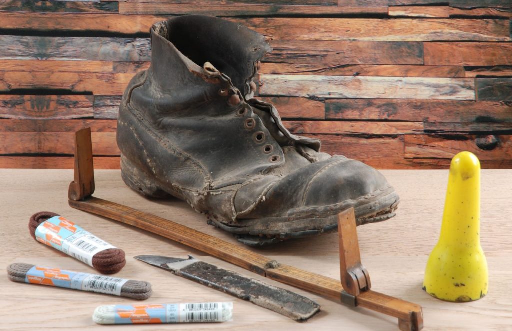 ein allter Schuh mit Schuhmacherwerkzeug und Schnürsenkeln daneben