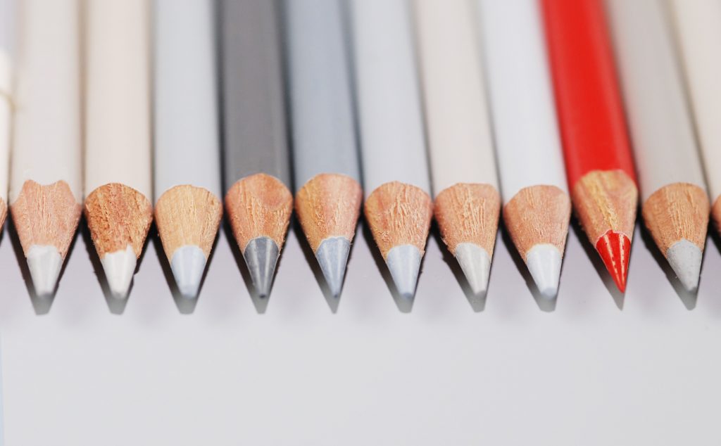 Schmuckfoto Buntstifte ein roter zwischen grauen Stiften